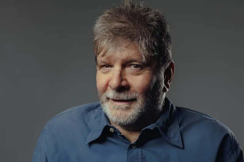 A studio portrait of author Marcelo Rubens Paiva in a blue shirt, from Netflix's press materials for the Happy Old Year adaptation