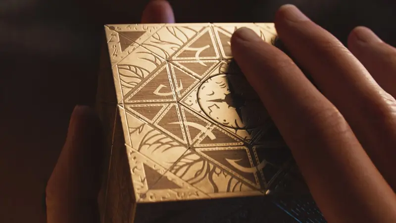 Hands turning the ornate gold Lament Configuration puzzle box, in artwork for Clive Barker's Hellraiser: Revival